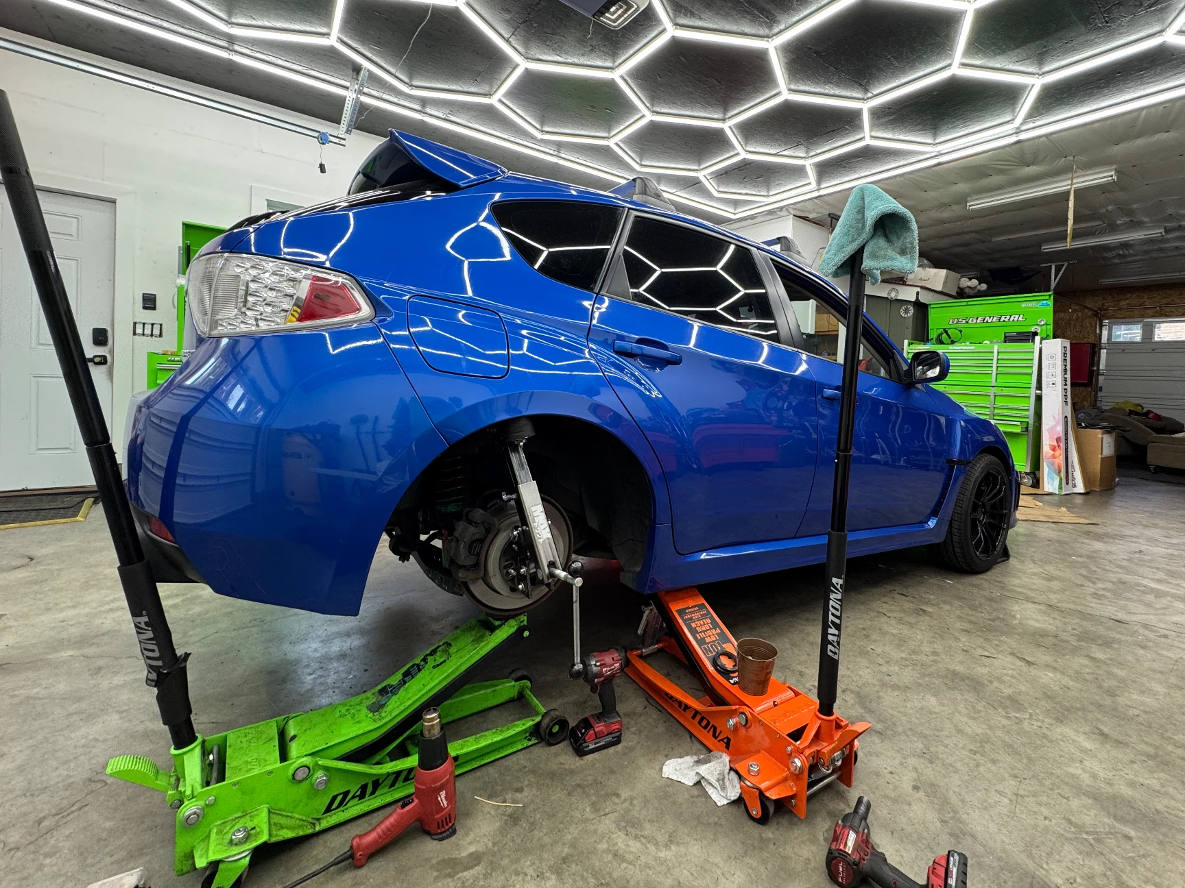 Blue Subaru WRX inside the shop with tools on the floor and hexagon ceiling lights overhead